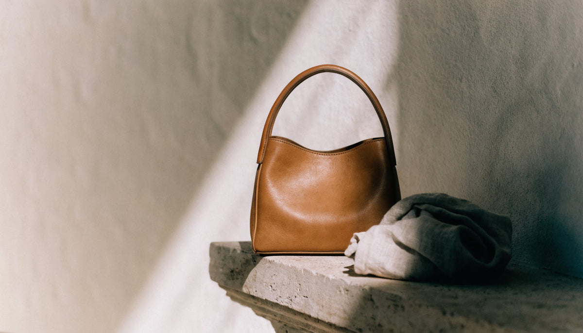 Tan leather handbag resting on a warm stone ledge beside linen in afternoon light — Vessa Bags